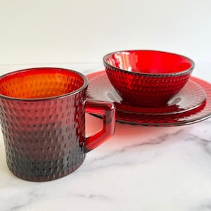 May include: A set of red glass dishes with a textured surface. The set includes a small bowl, a larger plate, and a cup.