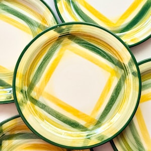 May include: Overhead view of several ceramic plates. Each plate has a white center with a yellow and green crisscross pattern. The rims are green. The plates are arranged in a circular pattern.