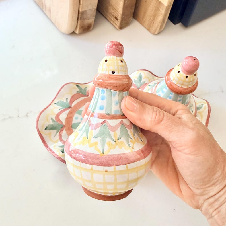 Pu&ograve; includere: Un set di saliera e pepiera in ceramica con un motivo dipinto a mano di linee a griglia gialle, strisce verticali azzurre e motivi a foglie verdi, sormontato da un pomello arrotondato rosa, su un vassoio ovale smerlato abbinato.