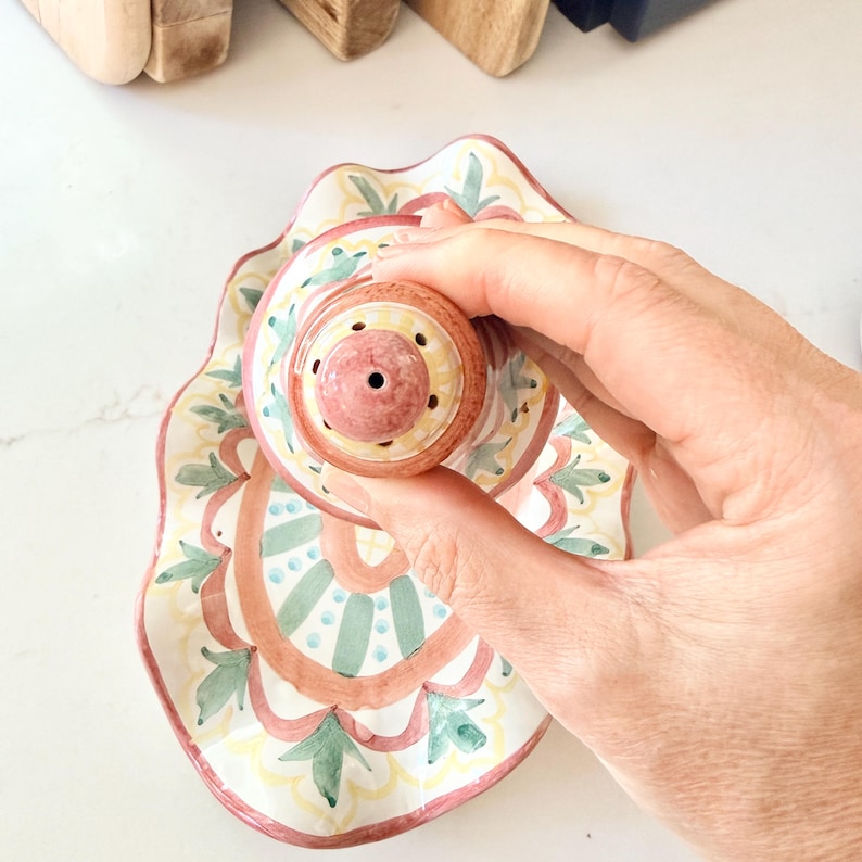 Pu&ograve; includere: Un salino o pepaiolo in ceramica con parte superiore arrotondata e vassoio smerlato abbinato. Il set presenta un motivo dipinto a mano nei toni del terracotta, verde salvia e giallo, con un foro centrale sul coperchio per l'uso.