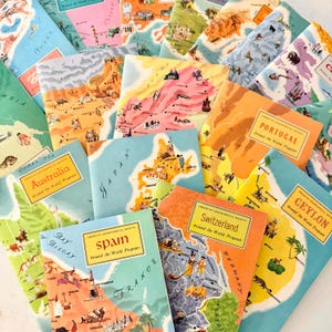 May include: A collection of vintage travel books from the American Geographical Society's "Around the World Program." The covers feature colorful illustrations of various countries, including Spain, Portugal, and Switzerland, with map-like designs and country names.