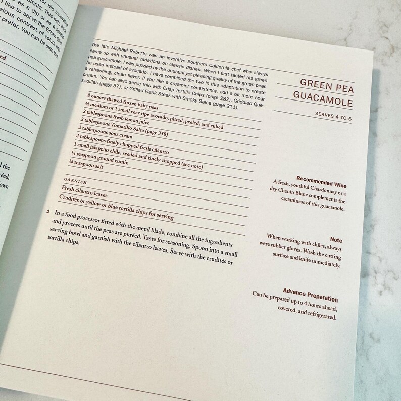 May include: Open cookbook page with a recipe for Green Pea Guacamole. The recipe includes ingredients like peas, avocado, lemon juice, and cilantro. The text also suggests serving with tortilla chips.