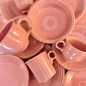 May include: A collection of pink ceramic dishes and mugs. The dishes have a ridged design and the mugs have a simple, rounded shape.