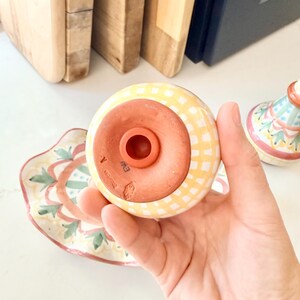 Pu&ograve; includere: Un dosatore in ceramica con un motivo a quadretti gialli e bianchi sull'esterno e una base color terracotta. La parte inferiore della base presenta un tappo in gomma circolare e marchi stampati tra cui la lettera A e altri simboli.
