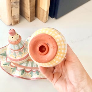 Pu&ograve; includere: Un set di saliera e pepiera in ceramica con motivo a quadretti gialli e bianchi. Un pezzo ha una forma a campana con base in terracotta e tappo, mentre l'altro &egrave; conico con una parte superiore rosa e dettagli verdi.