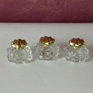 Conjunto de 3 pequenos frascos de perfume vintage da Avon, transparentes com tampas douradas.