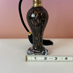 May include: A vintage perfume bottle with a black and brown speckled design. The bottle has a gold-colored top and a black cord with a tassel. The bottle is approximately 4 inches tall.