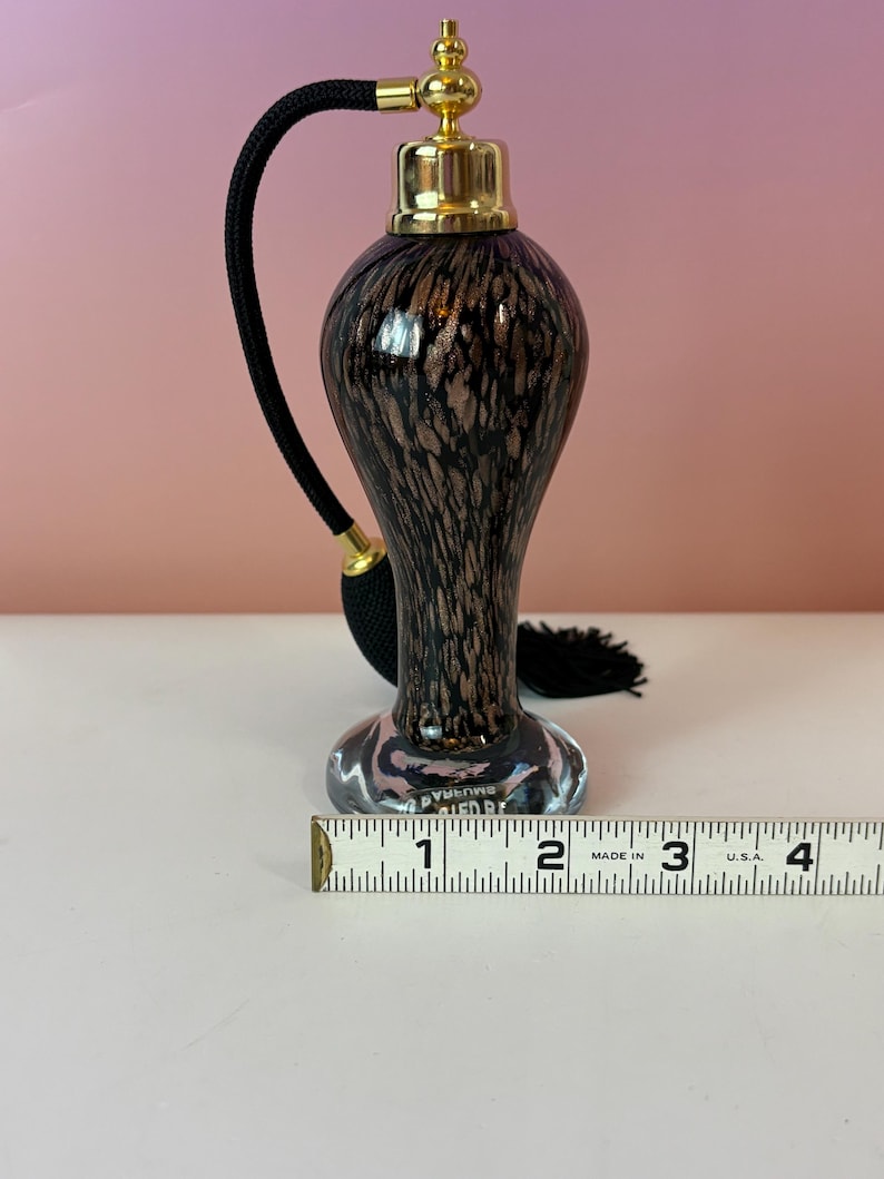 May include: A vintage perfume bottle with a black and brown speckled design. The bottle has a gold-colored top and a black cord with a tassel. The bottle is approximately 4 inches tall.