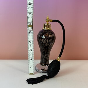 May include: A vintage perfume bottle with a black and brown speckled design. The bottle has a gold-colored top and a black bulb atomizer with a black tassel. The bottle is approximately 6 inches tall.