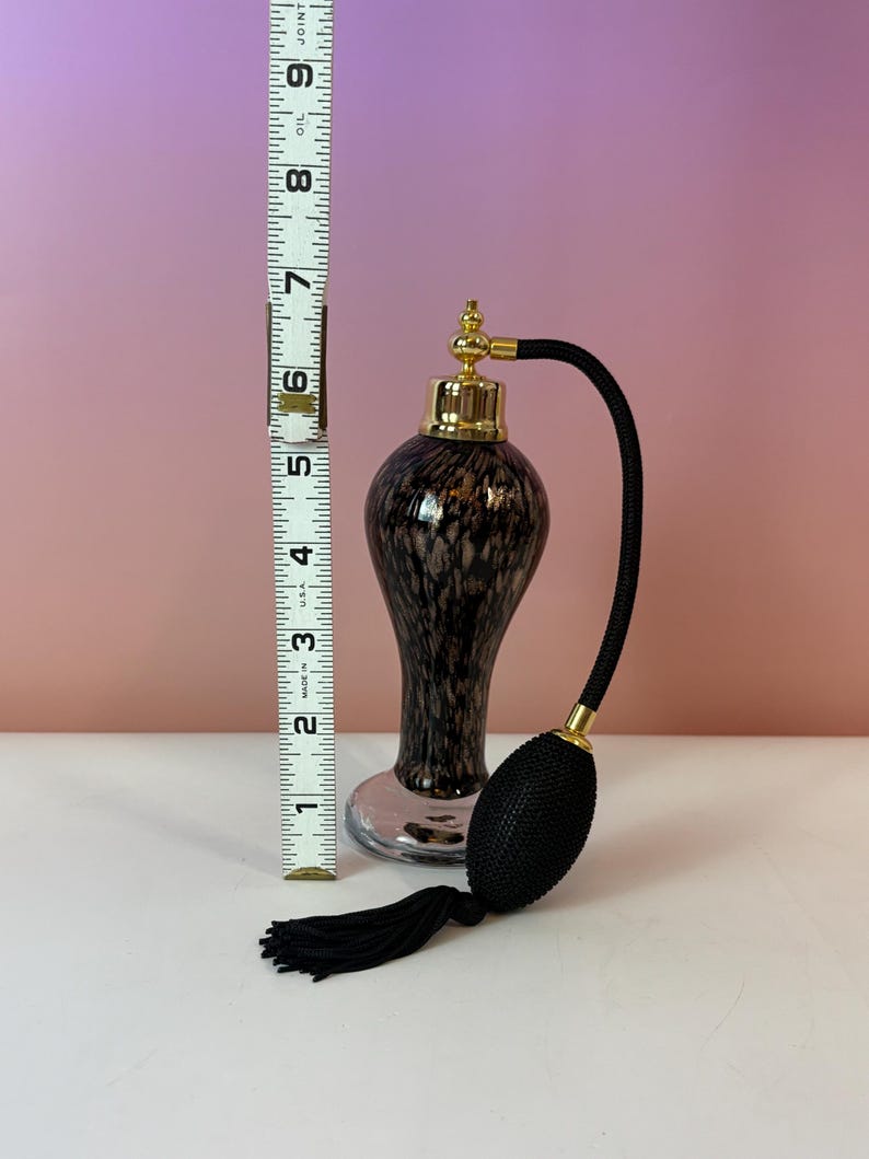 May include: A vintage perfume bottle with a black and brown speckled design. The bottle has a gold-colored top and a black bulb atomizer with a black tassel. The bottle is approximately 6 inches tall.