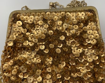 May include: A gold sequined evening bag with a chain strap. The bag is covered in small, round sequins and has a delicate, feminine design.