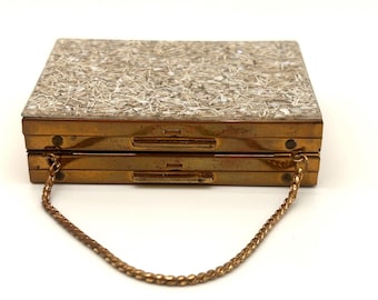 May include: A vintage rectangular clutch with a gold-tone metal frame and a textured, sparkly top. The clutch has a chain strap and a clasp closure. The top is covered in a mosaic of small, light-colored pieces.