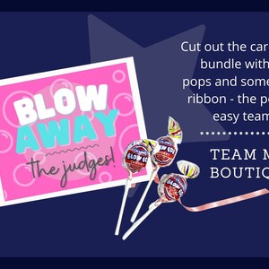 Puede incluir: Una tarjeta rosa con el texto "Blow Away the judges!" y una cinta rosa. Tres piruletas con envoltorios coloridos est&aacute;n en la esquina inferior derecha. El texto "TEAM MOM BOUTIQUE" est&aacute; en la esquina inferior derecha.