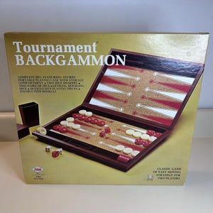 Puede incluir: Un juego de Backgammon Tournament en una caja. El tablero de juego abierto es marrón con triángulos rojos y blancos. El juego incluye dados, fichas y cubiletes. La caja tiene el texto "Tournament Backgammon".