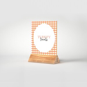 Puede incluir: Un letrero de madera con un patrón de cuadros de color melocotón y blanco y un círculo blanco con el texto "TURKEY treats" en negro.