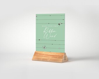 May include: A light green sign with a wooden stand that says "Make your own Ribbon Wand" with a floral pattern.