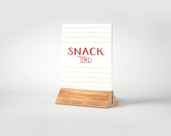 May include: A white sign with gold stripes and the text "SNACK TIME!" in red lettering. The sign is on a wooden stand.