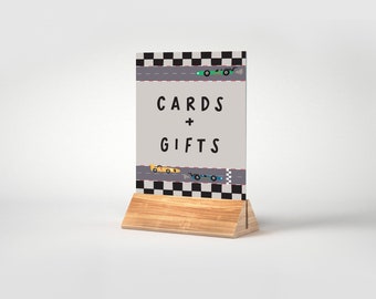 Peut inclure: Un panneau en bois avec un design de piste de course à damier et des voitures de course dessinées. Le panneau indique "CARDS + GIFTS".