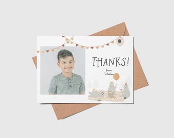 May include: A thank you card featuring a photo of a smiling child, with the word "THANKS!" in a whimsical font. The card includes illustrations of bears, a picnic scene, and a banner. The card is paired with a brown envelope.