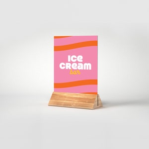 May include: A pink and orange striped sign with the text "Ice Cream Bar" in white and yellow letters. The sign is on a wooden stand.