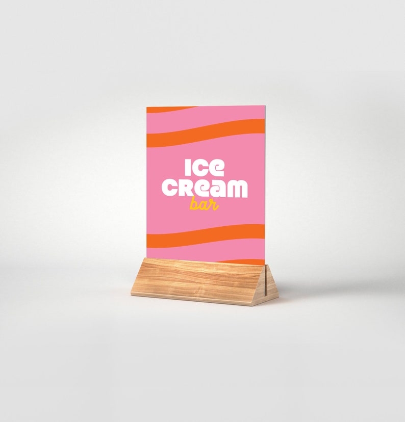 May include: A pink and orange striped sign with the text "Ice Cream Bar" in white and yellow letters. The sign is on a wooden stand.