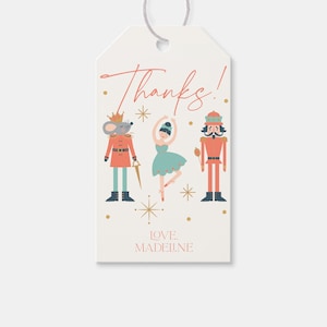 Puede incluir: Una etiqueta de regalo blanca con un mensaje rojo "¡Gracias!" La etiqueta presenta un Cascanueces, una bailarina y un rey ratón en una ilustración caprichosa. Estrellas doradas y puntos decoran el fondo. El texto "LOVE, MADELINE" está en la parte inferior de la etiqueta.