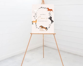 May include: Welcome to Emma's 4th Birthday Party! A pink sign with a white border features a wreath of flowers and five horses in different poses. The sign is displayed on a wooden easel.