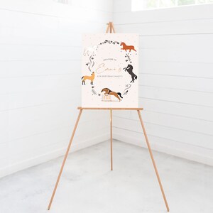 May include: Welcome to Emma's 4th Birthday Party! A pink sign with a white border features a wreath of flowers and five horses in different poses. The sign is displayed on a wooden easel.