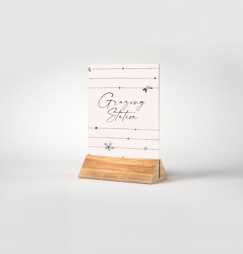May include: A white sign with black text and floral accents that reads "Grazing Station" on a wooden stand.