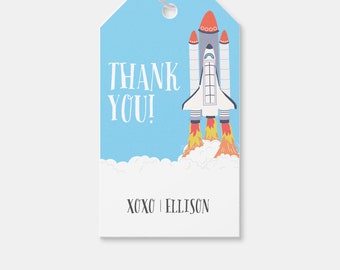 May include: A blue thank you tag with a white rocket ship launching into a white cloud. The text "THANK YOU! XOXO ELLISON" is printed on the tag.