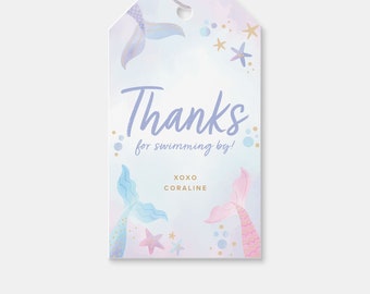 Puede incluir: Una etiqueta de agradecimiento azul claro y morado con un diseño de cola de sirena. La etiqueta dice "Gracias por nadar por aquí! XOXO Coraline".