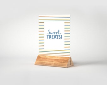 May include: A white sign with colorful stripes and the text "Sweet Treats!" in blue lettering. The sign is on a wooden stand.