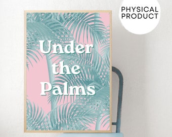 May include: A framed art print featuring a pink background with teal palm fronds. The words "Under the Palms" are printed in white. The print is displayed on a light blue chair.