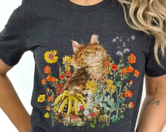 以下が含まれることがあります： ヘザーダークグレーのTシャツに、カラフルな野花畑に座っている茶トラ猫のグラフィックがプリントされています。