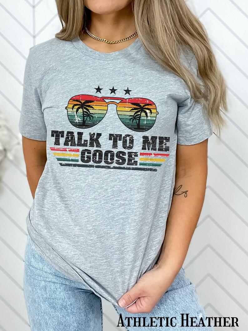 May include: A heather grey t-shirt with a retro-style graphic of sunglasses with palm trees and the text "TALK TO ME GOOSE".