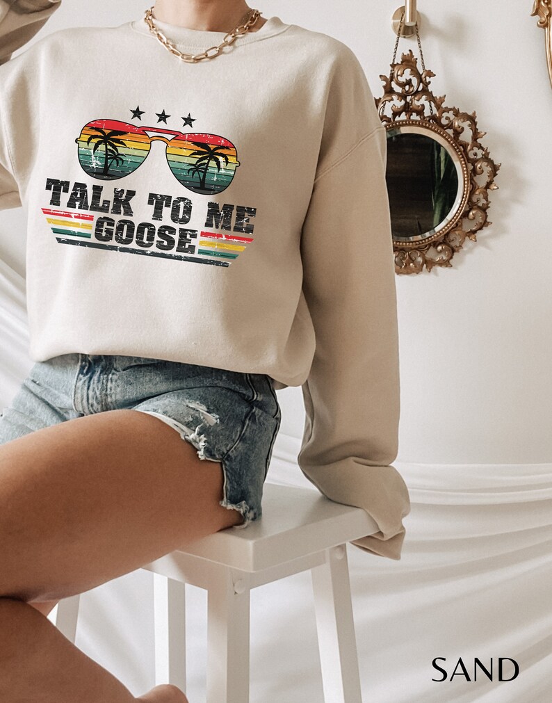 以下が含まれることがあります： パームツリーが描かれたサングラスと「Talk to me Goose」というテキストがレトロなスタイルでプリントされたベージュのトレーナーです。