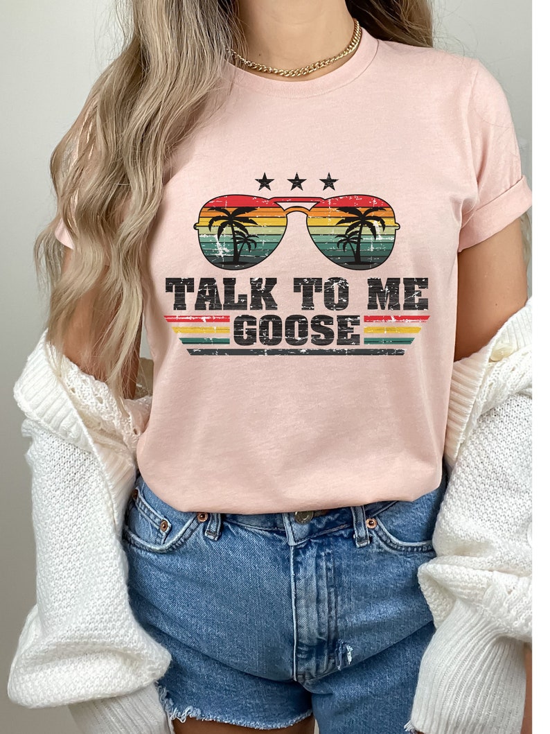 May include: A pink t-shirt featuring a retro-style graphic of sunglasses with palm trees reflected in the lenses. The text "TALK TO ME GOOSE" is printed below the sunglasses.
