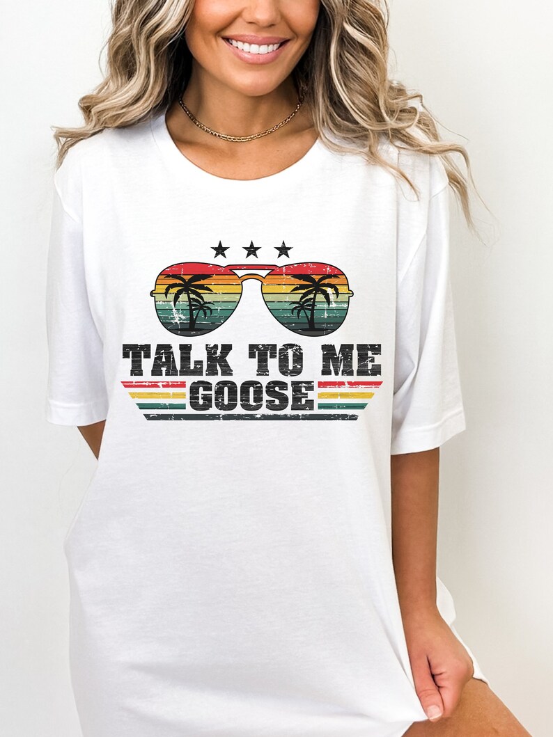 May include: White t-shirt featuring a retro-style graphic of sunglasses with palm trees reflected in the lenses. The text "TALK TO ME GOOSE" is printed below the sunglasses.