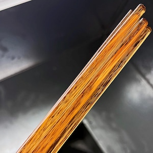 May include: Close-up of several amber-colored, rectangular rods. The rods have a wood-grain appearance and are arranged in a parallel fashion. The background is a dark gray color with a fan visible.