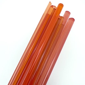 May include: A bundle of translucent orange glass rods, arranged diagonally against a white background. The rods vary slightly in shade, creating a gradient effect. The ends of the rods are rounded.