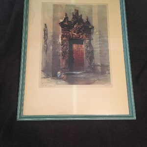 May include: A framed print featuring a detailed architectural rendering of a doorway with a red door. The print is set within a light green wooden frame. The artwork showcases intricate carvings and a sense of depth.