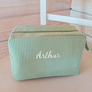 Op de afbeelding: Een groen-wit gestreepte toilettas met een ritssluiting. De tas is gepersonaliseerd met de naam "Arthur" in witte letters.