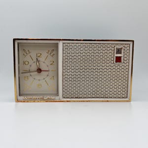 May include: A vintage Westclox alarm clock with a gold-coloured frame. The clock face is white with gold numerals and hands. The right side features a textured silver panel and a red and white date indicator. The clock is rectangular.