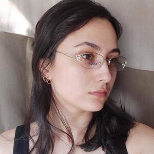 May include: A woman with long dark hair wearing a black tank top and clear framed glasses with the word "BLUE" printed on the frame.