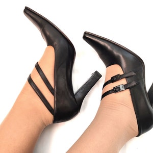 May include: A pair of black leather high-heeled shoes with ankle straps and buckles. The shoes have a pointed toe and a chunky heel.