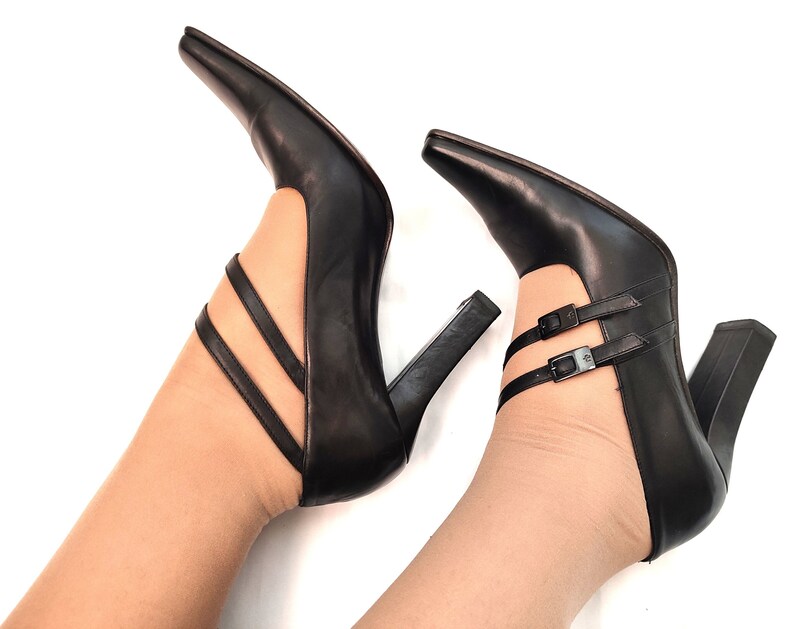 May include: A pair of black leather high-heeled shoes with ankle straps and buckles. The shoes have a pointed toe and a chunky heel.