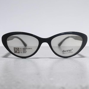 Op de afbeelding: Zwarte cat-eye bril met heldere glazen. Het rechterglas bevat een QR-code en numerieke gegevens, terwijl het linkerglas de tekst 'diverso Memory Eyewear' toont. Het montuur heeft een gladde, glanzende afwerking en een kenmerkende puntige vorm.