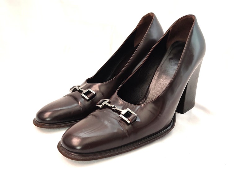 May include: A pair of brown leather heeled pumps with silver buckle accents.