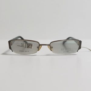Op de afbeelding: Bruine metalen bril met een rechthoekig montuur. Het rechterglas is voorzien van een sticker met een QR-code, terwijl op het linkerglas de tekst HEROS EYEWEAR staat. Het modelnummer HR50541 50-19 is zichtbaar op het rechterglas.