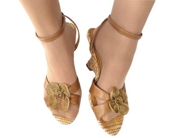 May include: Tan leather sandals with a woven platform heel and a gold flower embellishment on the toe strap.